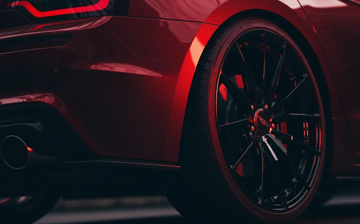 Detaliu al unei mașini sport roșii echipate cu jante auto premium negre lucioase. Iluminarea roșie accentuează designul elegant și calitatea jantelor auto și a cauciucurilor.